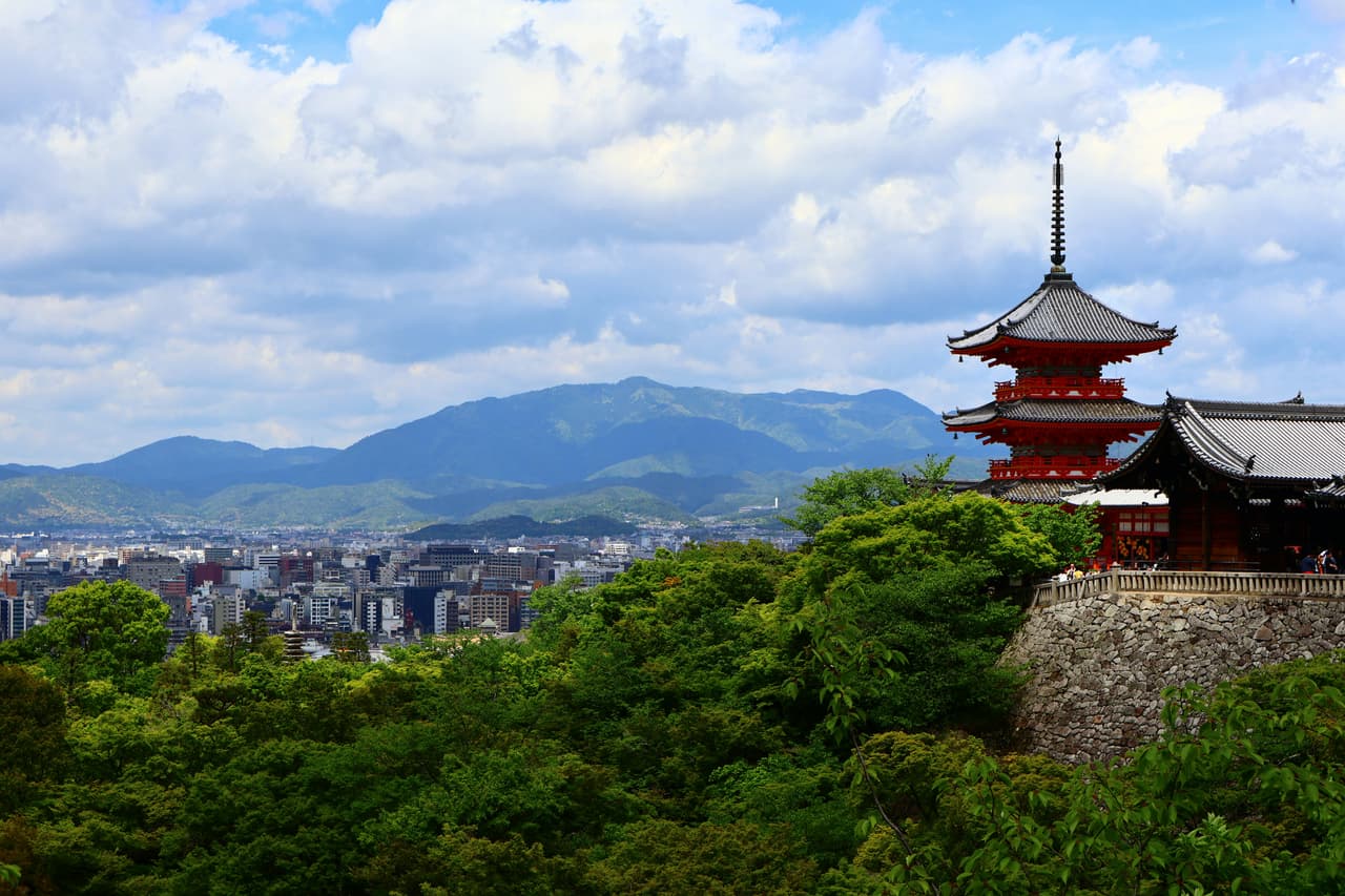 Historische Pagode über Kyoto, dahinter die moderne Stadt und bewaldete Berge - Foto von Cristina Aragon auf Unsplash